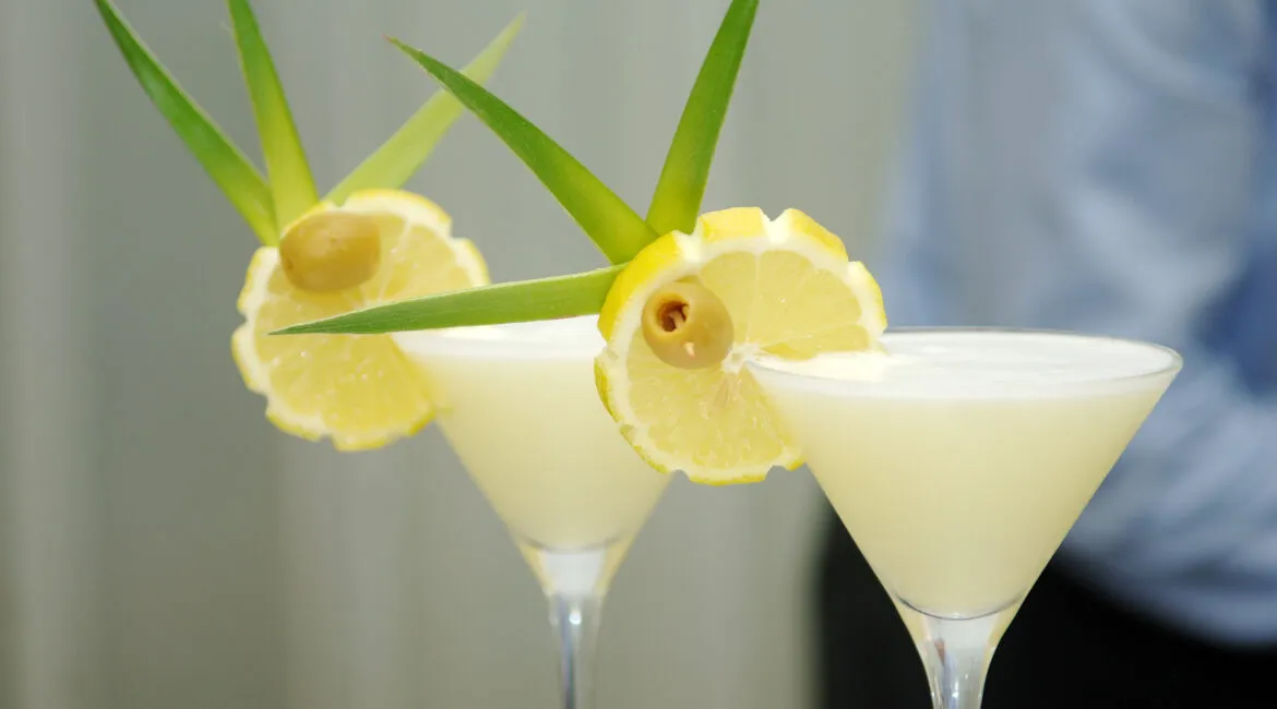 Two pale cocktails garnished with lemon and olives